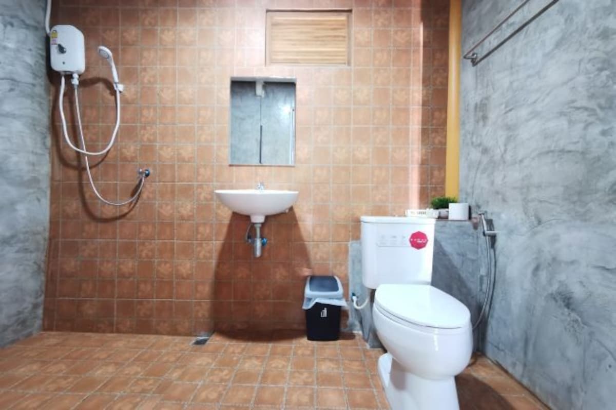 A bathroom with a shower, sink, toilet, and a small trash bin.