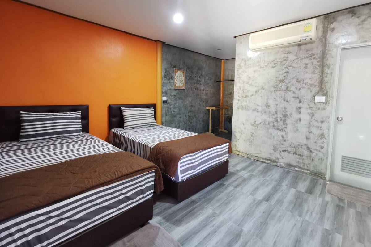 A hotel room with two beds, an orange wall, a marble wall, and a door with an air conditioning unit.