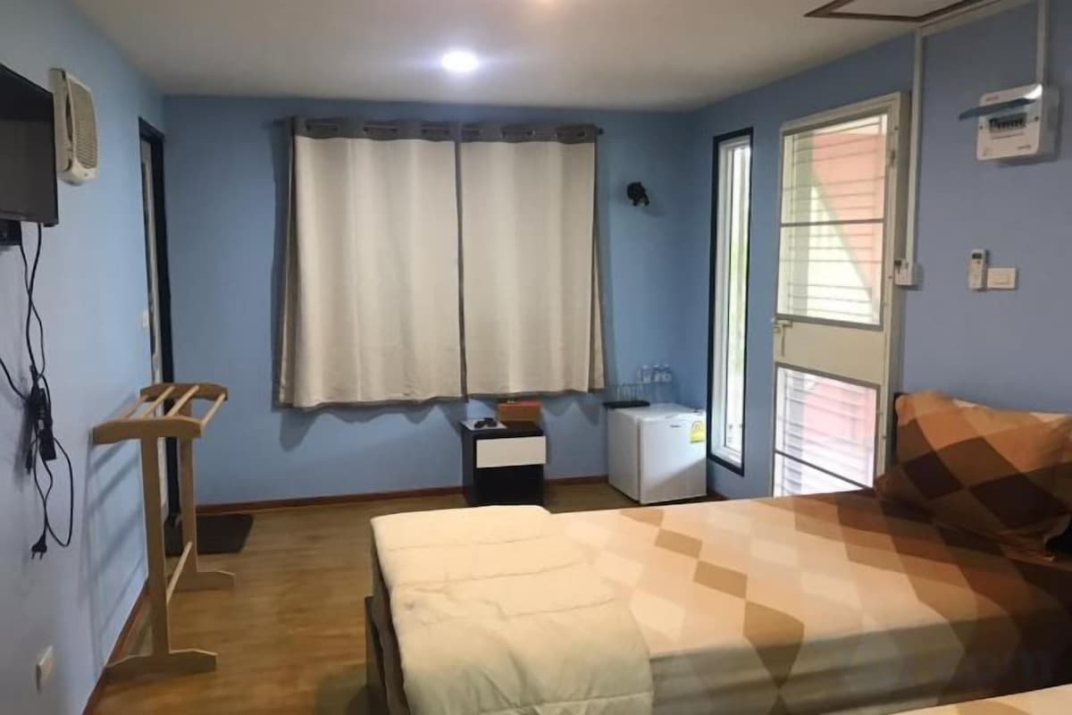 A bedroom with a bed, a desk, a chair, a window with curtains, and a wall-mounted television.