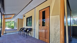 A covered outdoor area with a tiled floor, a wooden door, and a window with a view of greenery. - Viman Resort (Si Racha)