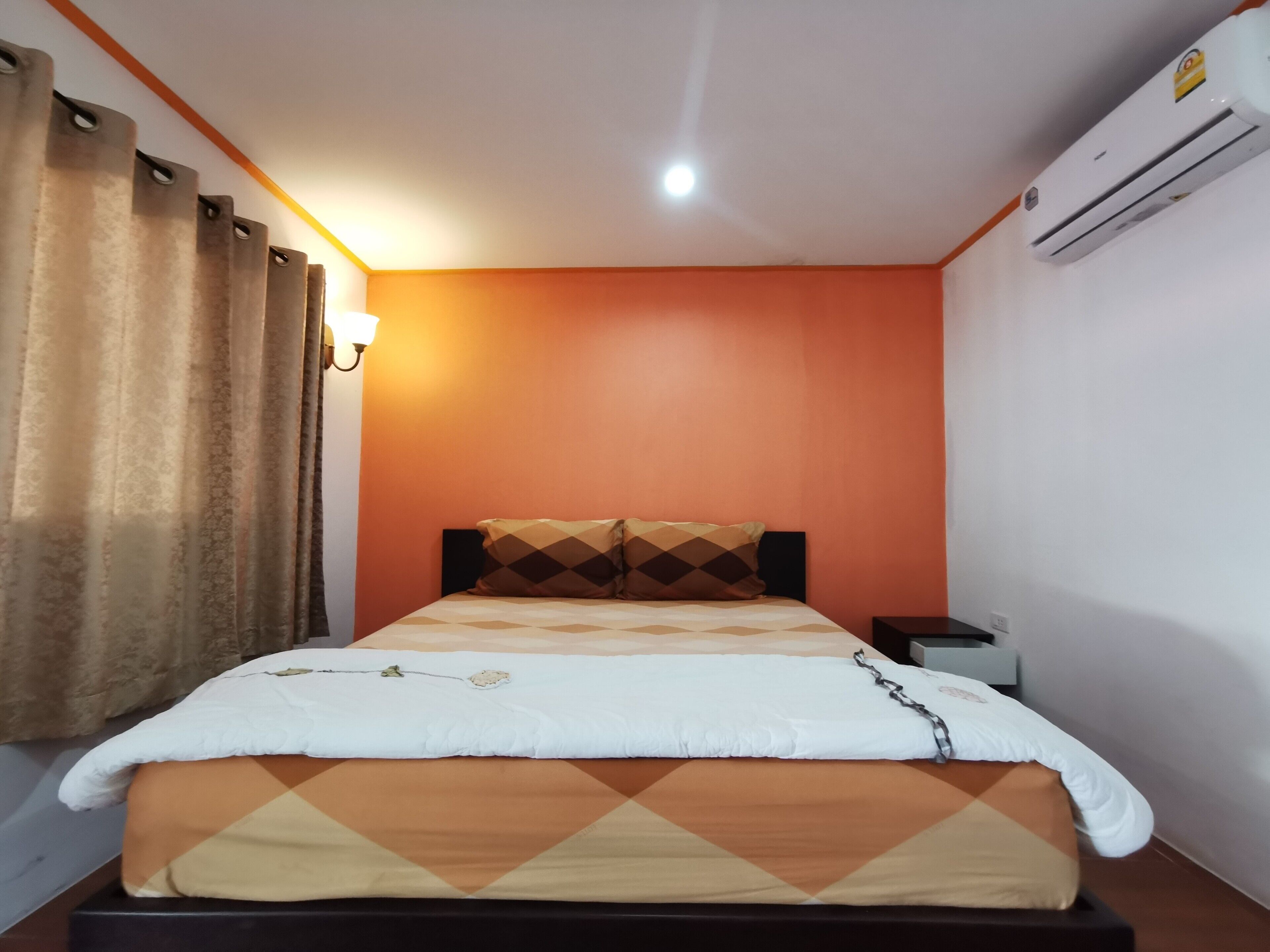 Une chambre d’hôtel équipée d’un lit, d’un climatiseur, d’une table de chevet et d’une lampe fixée au mur.