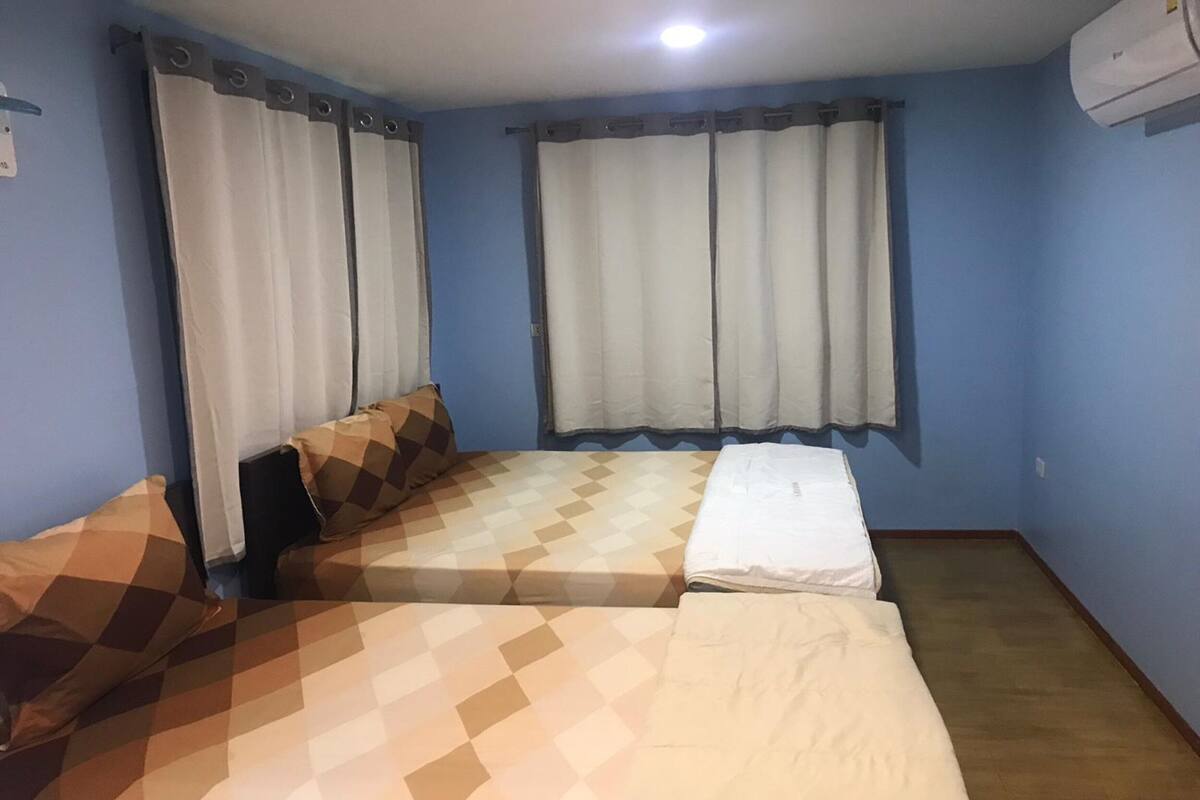 A room with two beds, a window with curtains, and an air conditioning unit on the wall.