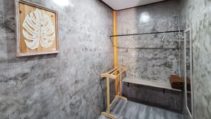 A bathroom with a concrete wall, a wooden leaf artwork, a towel rack, and a shelf with towels. - Viman Resort (Si Racha)
