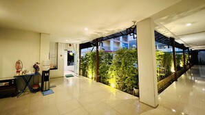 A hotel lobby with a tiled floor, a reception desk, and a view of a building with balconies. - INN Kham Apartment (Chiang Mai)