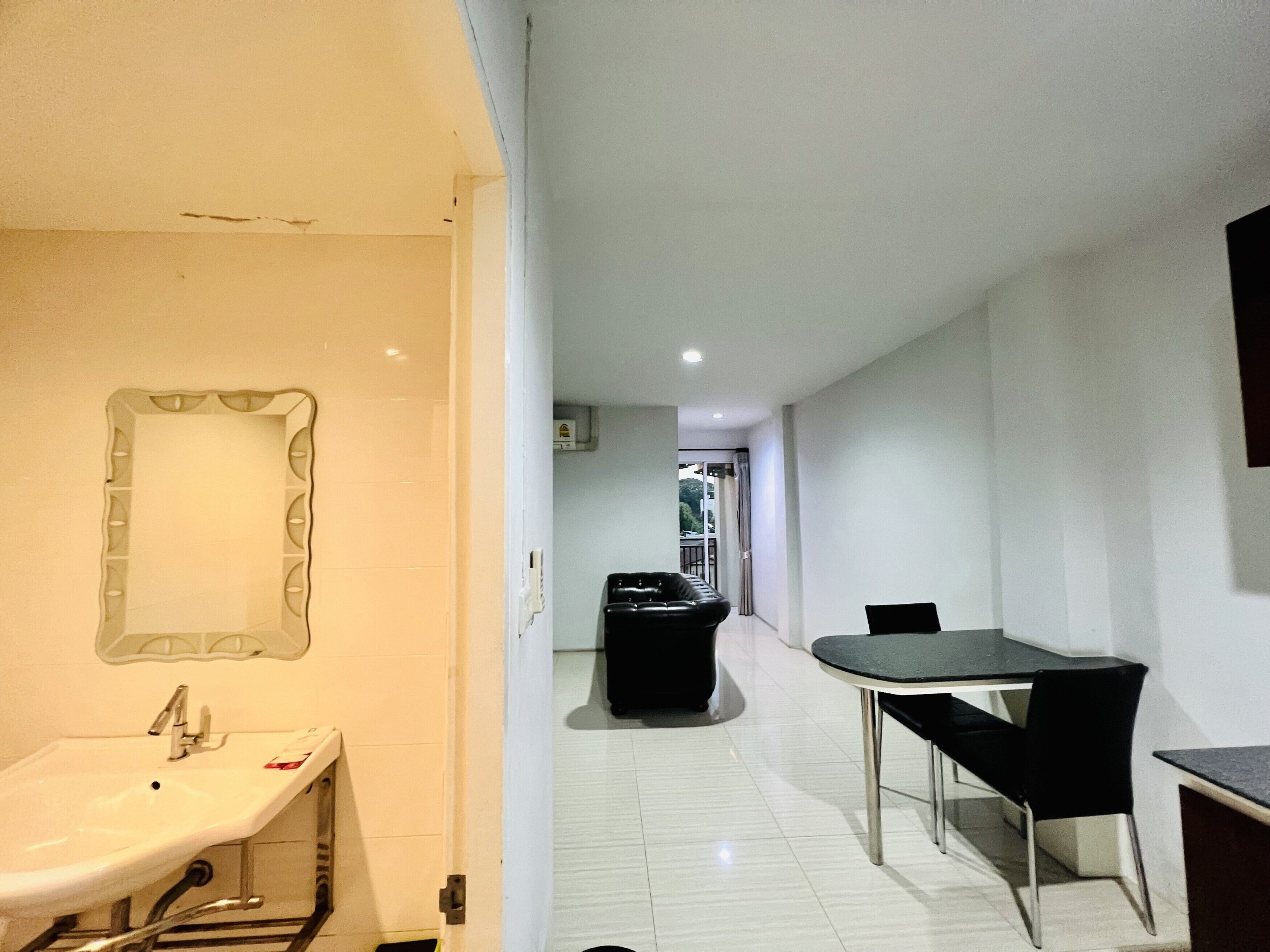 A hotel room with a bathroom, a dining area with a table and chairs, and a corridor leading to another room.