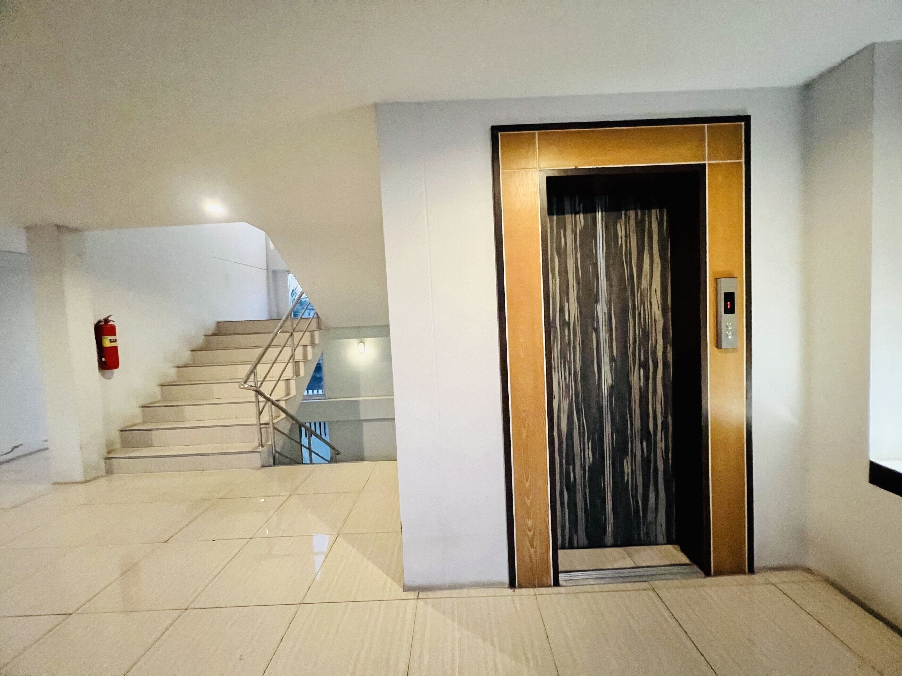 A modern interior with a staircase, a fire extinguisher, and an elevator.