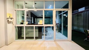 A modern interior with a large sliding glass door leading to a dining area. There are multiple shelves with items on display, and a small table with chairs in the dining area. - INN Kham Apartment (Chiang Mai)