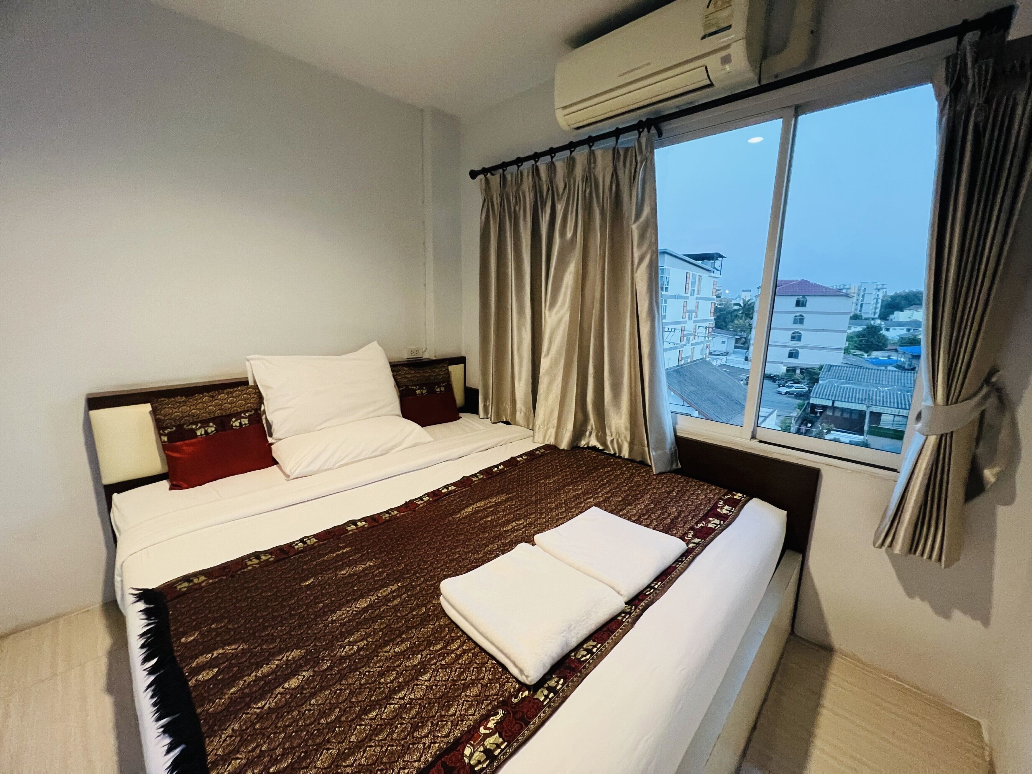 Une chambre d’hôtel avec un grand lit, une fenêtre avec des rideaux et un appareil de climatisation.