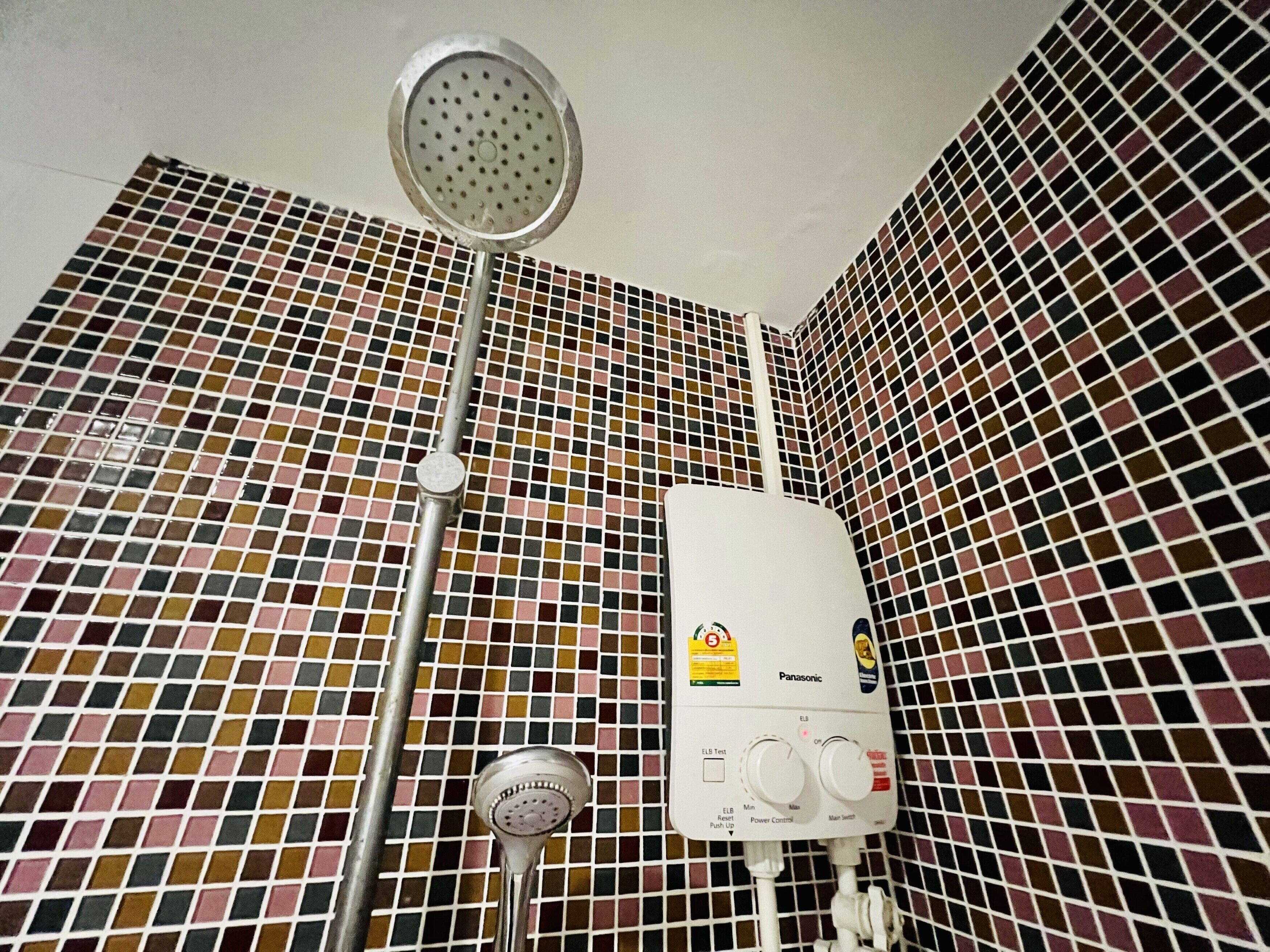 A bathroom with a tiled wall, a showerhead, and a water heater.