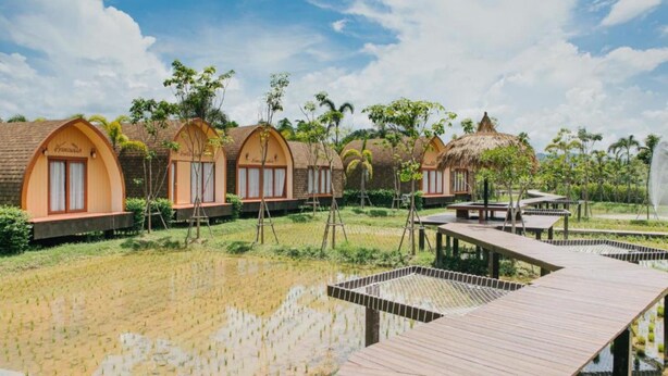 Una hilera de cabañas de madera con techos arqueados, rodeadas por una masa de agua y vegetación.