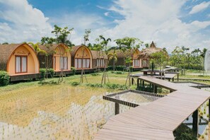 A row of wooden cottages with arched roofs, surrounded by a water body and greenery. - Srida Resort Lanna & Cafe (Doi Saket)