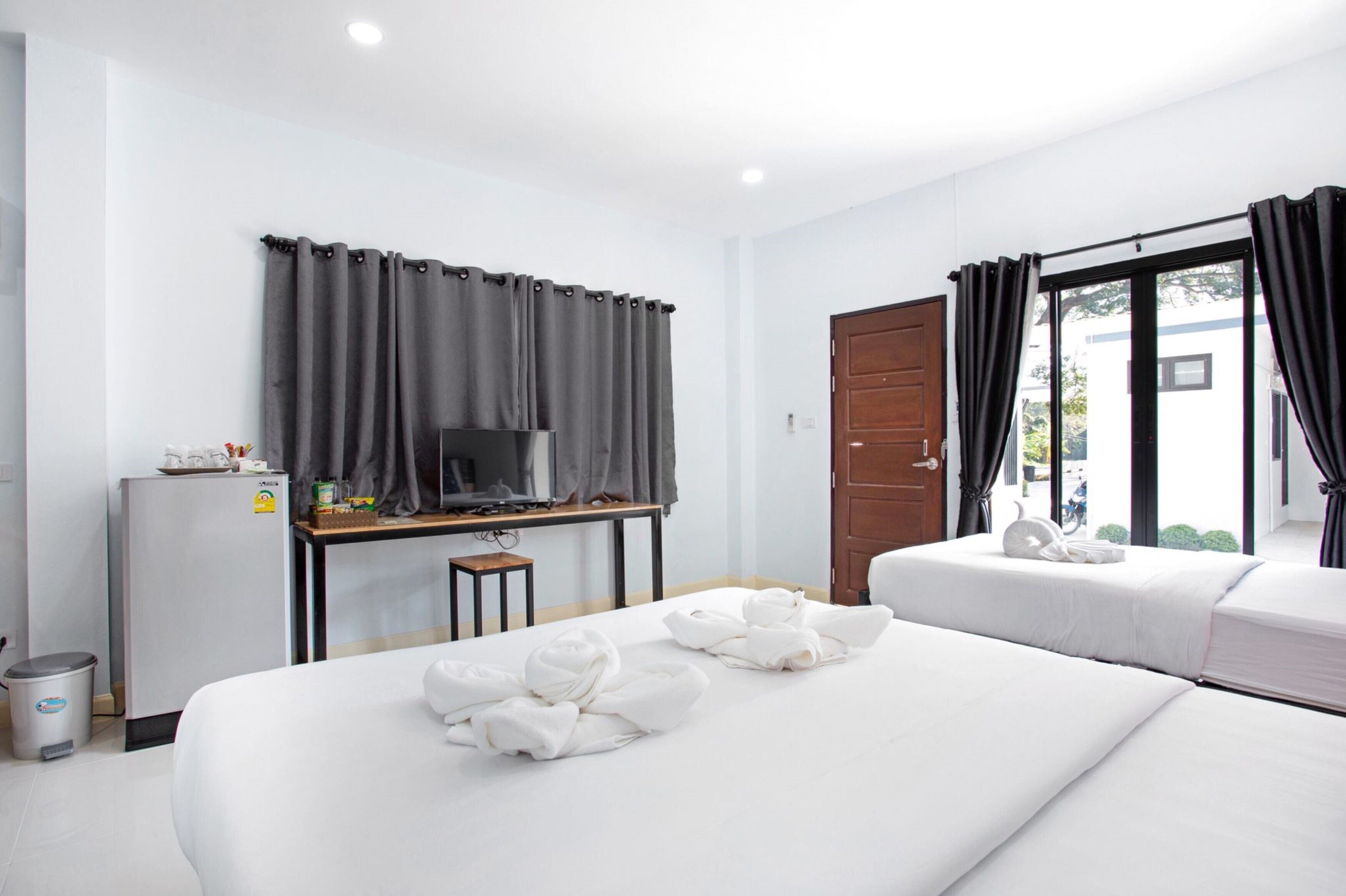 Habitación de hotel con dos camas, un televisor, un escritorio con computadora y una puerta que da a un balcón.