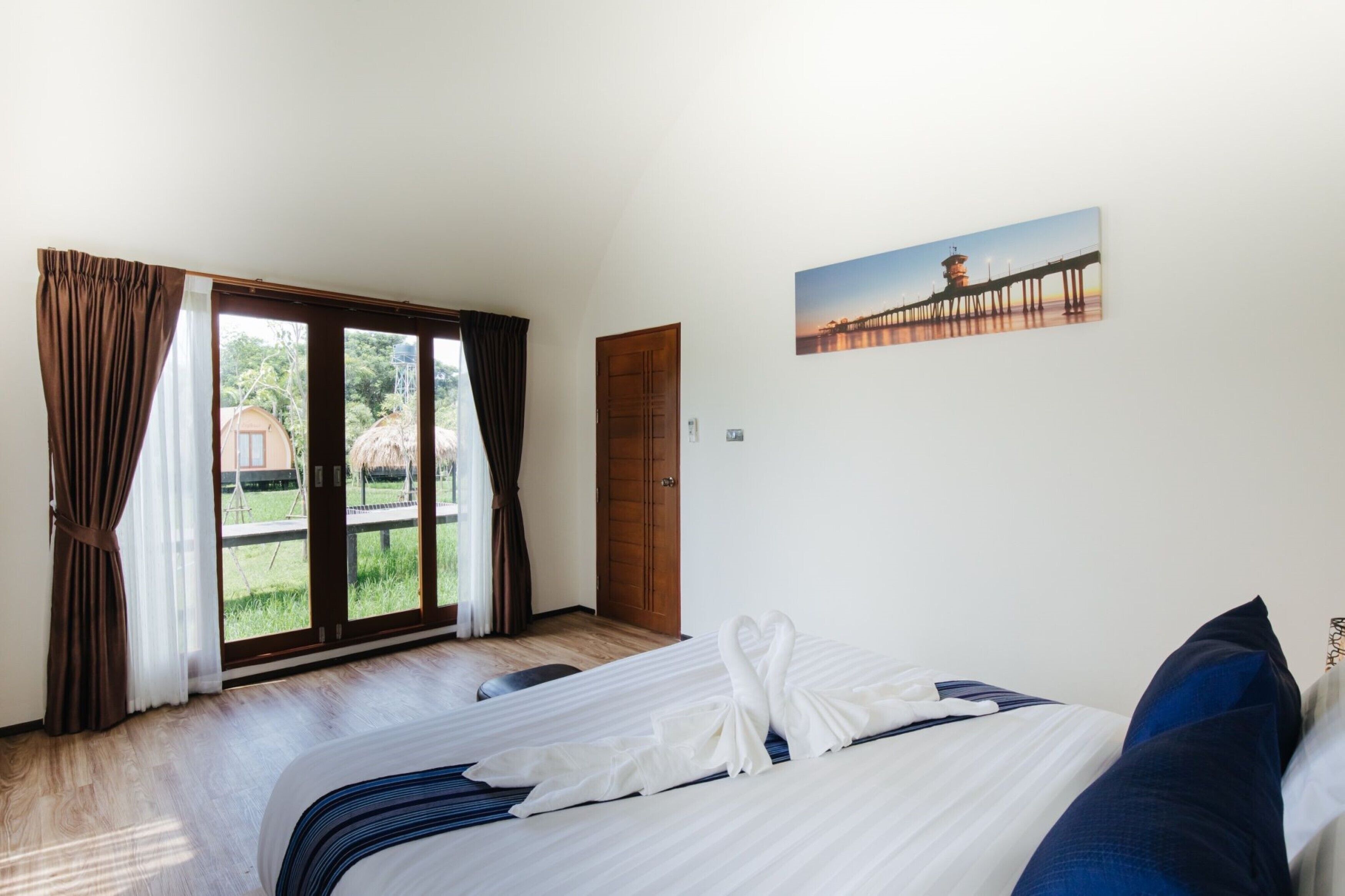 Habitación de hotel con una cama, un cuadro de un muelle y vistas a través de la puerta de cristal.