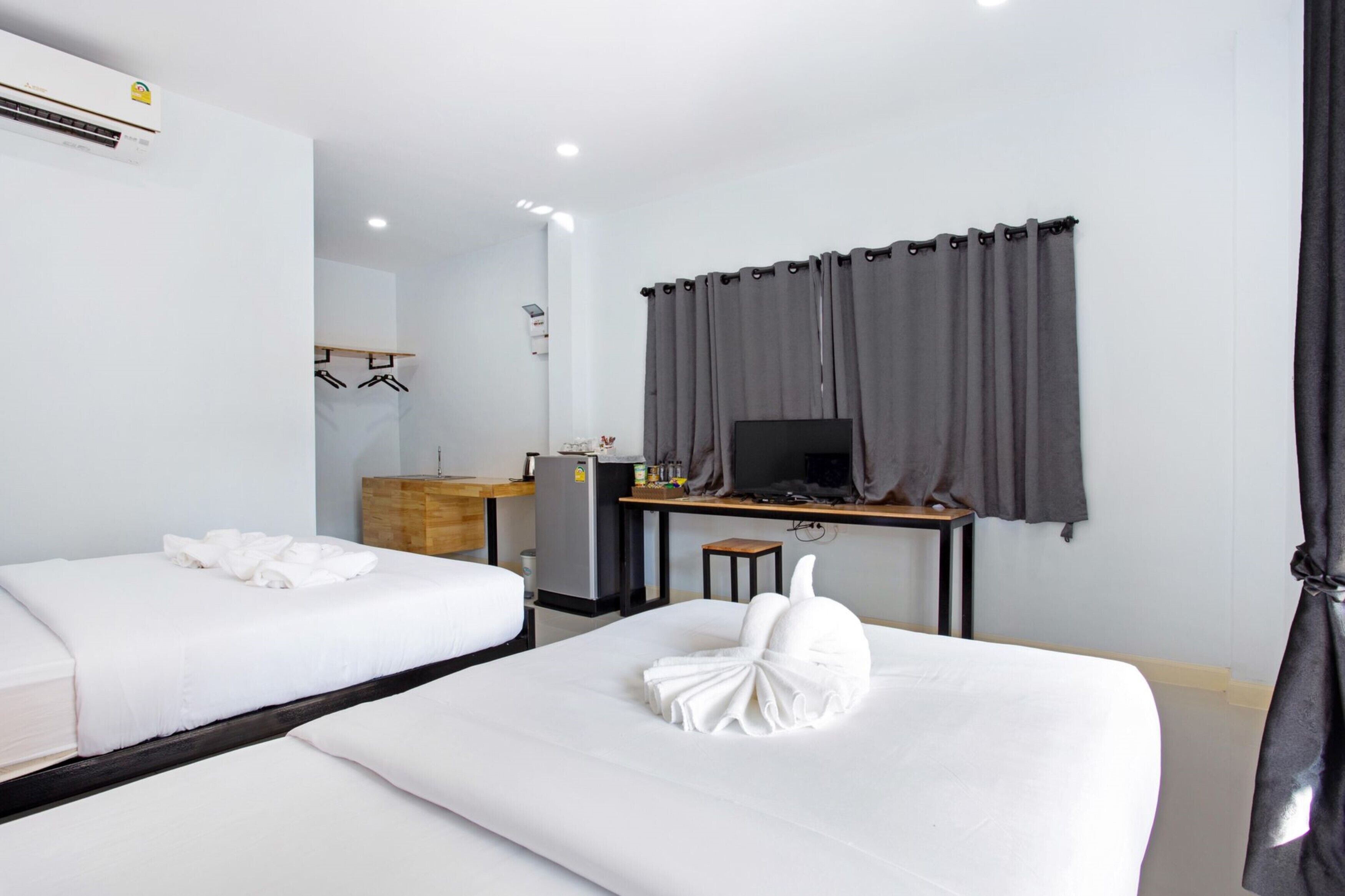 Habitación de hotel con dos camas, un escritorio con computadora, un refrigerador pequeño y un espejo.