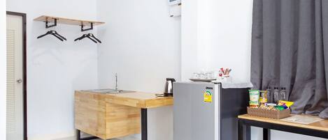 A compact kitchenette with a wooden countertop, a sink, a refrigerator, and a small table with snacks.