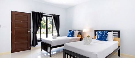 A hotel room with two beds, a wooden door, a window with black curtains, and a white wall.