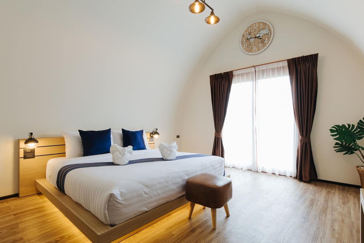 Ein modernes Schlafzimmer mit einem hölzernen Bett, einer Nachttischlampe, einer Wanduhr und einem großen Fenster mit Vorhängen.