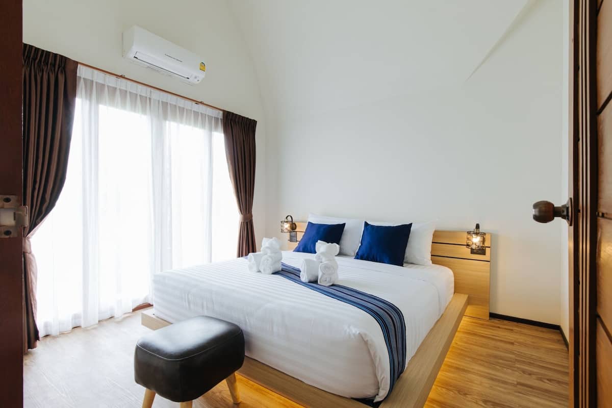 Ein Hotelzimmer mit einem großen Bett, zwei Nachttischen, einer Klimaanlage, einem Fenster mit Vorhängen und einem Holzboden.