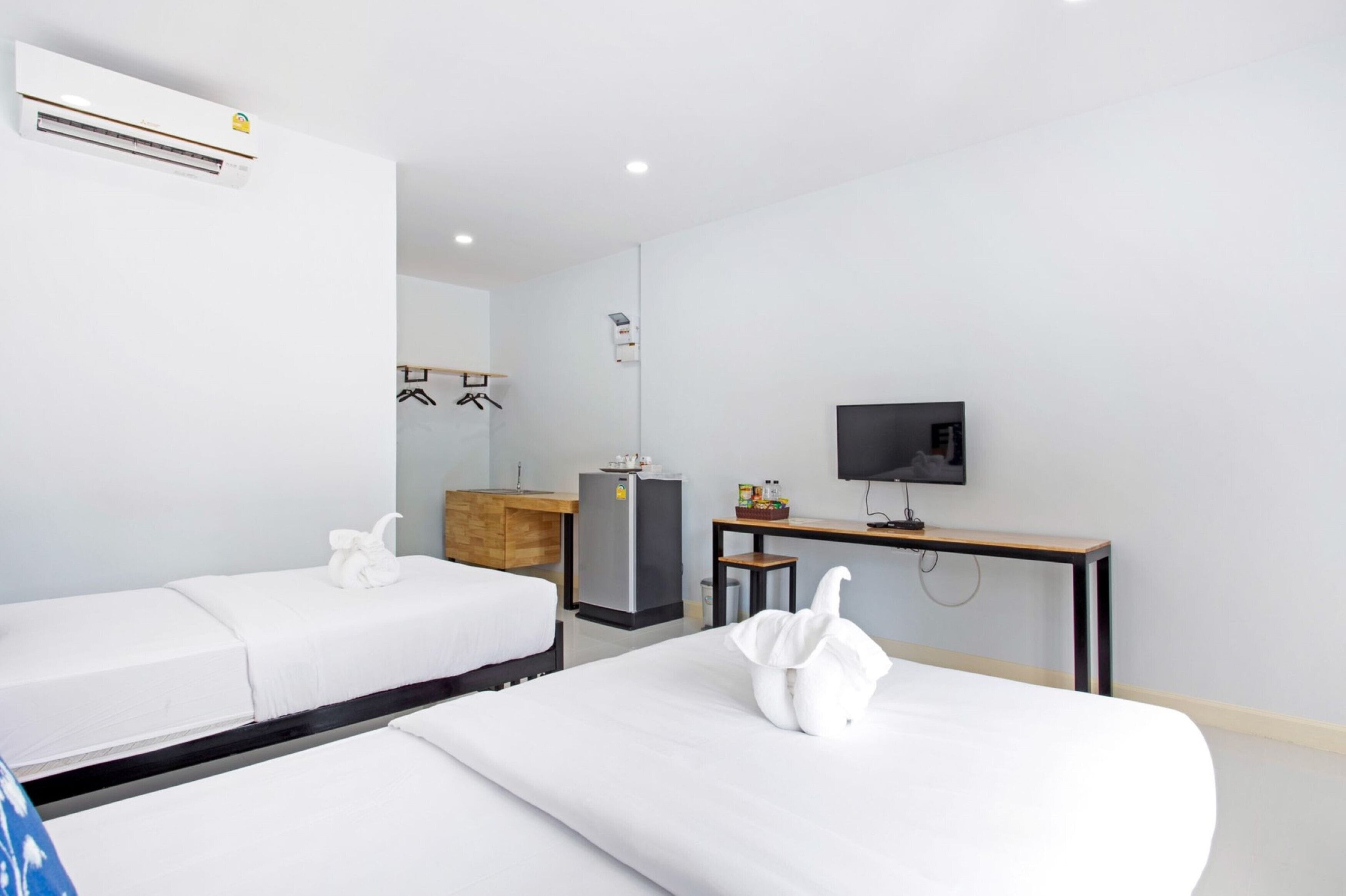 Une chambre d’hôtel avec deux lits, un bureau, une télévision, une armoire et un mini-bar.