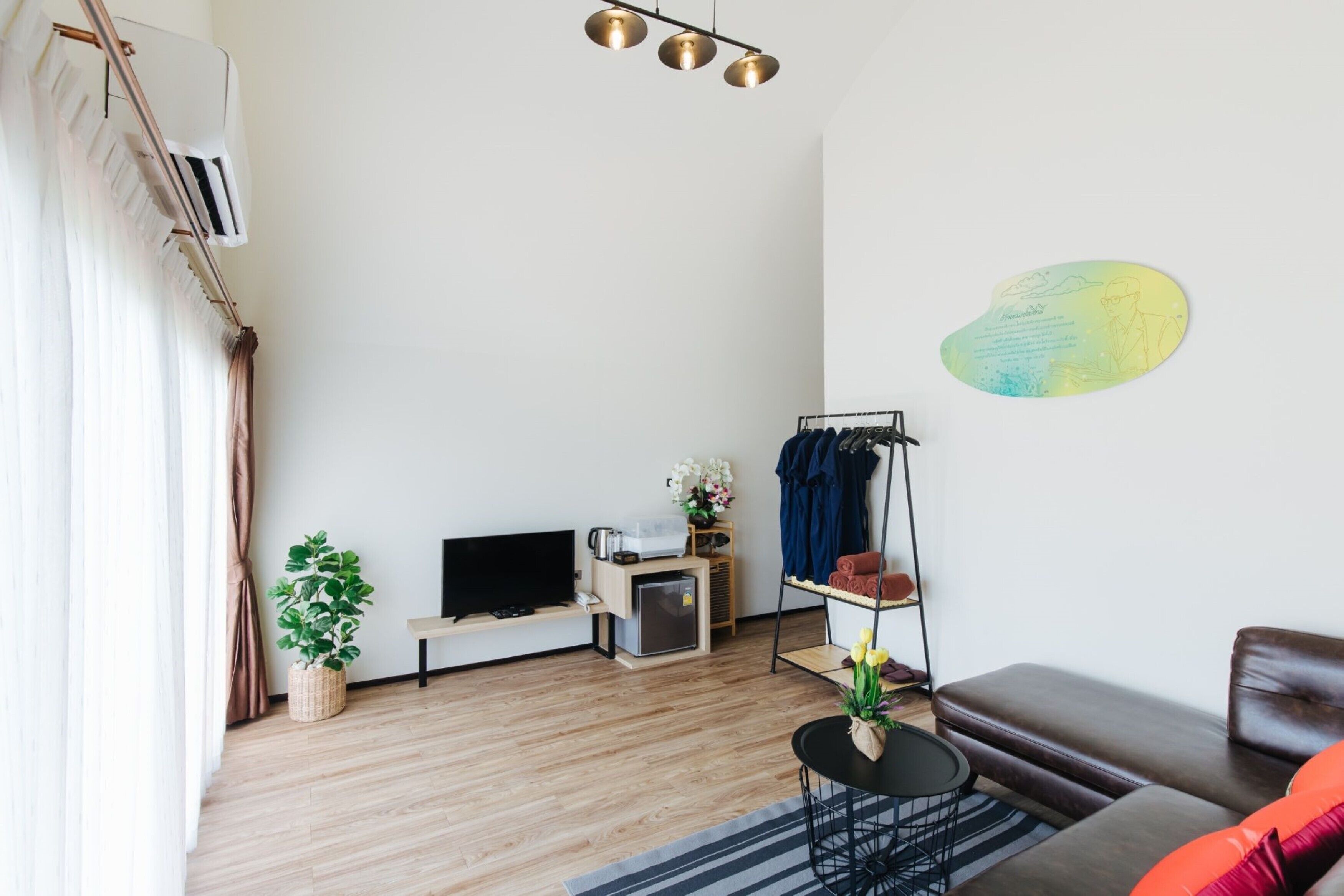 A modern living room with a flat-screen TV, a small table with a plant, a sofa, and a wall-mounted shelf with clothes and a vase of flowers.