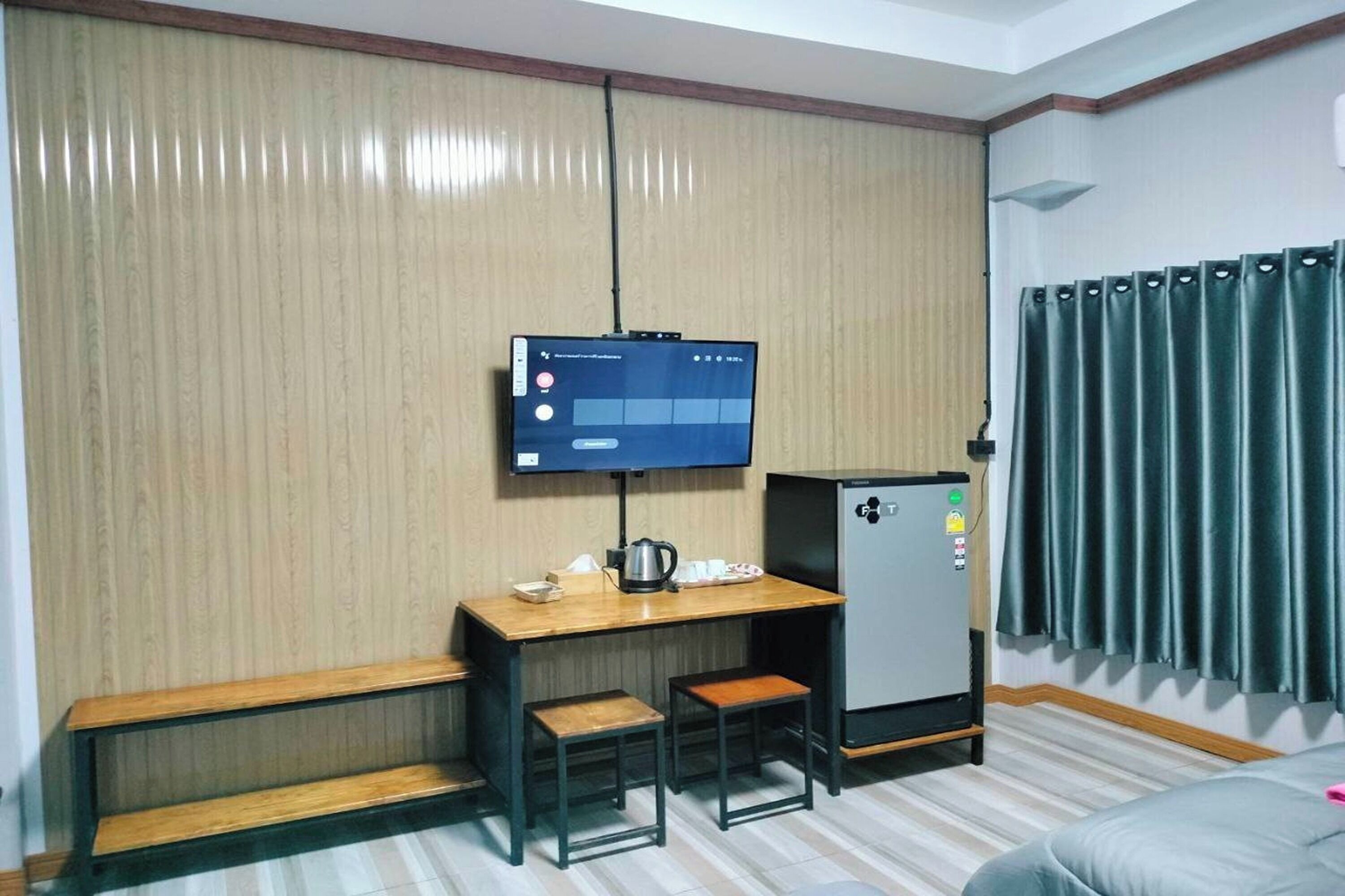 A hotel room with a bed, a desk with two chairs, a television, and a refrigerator.