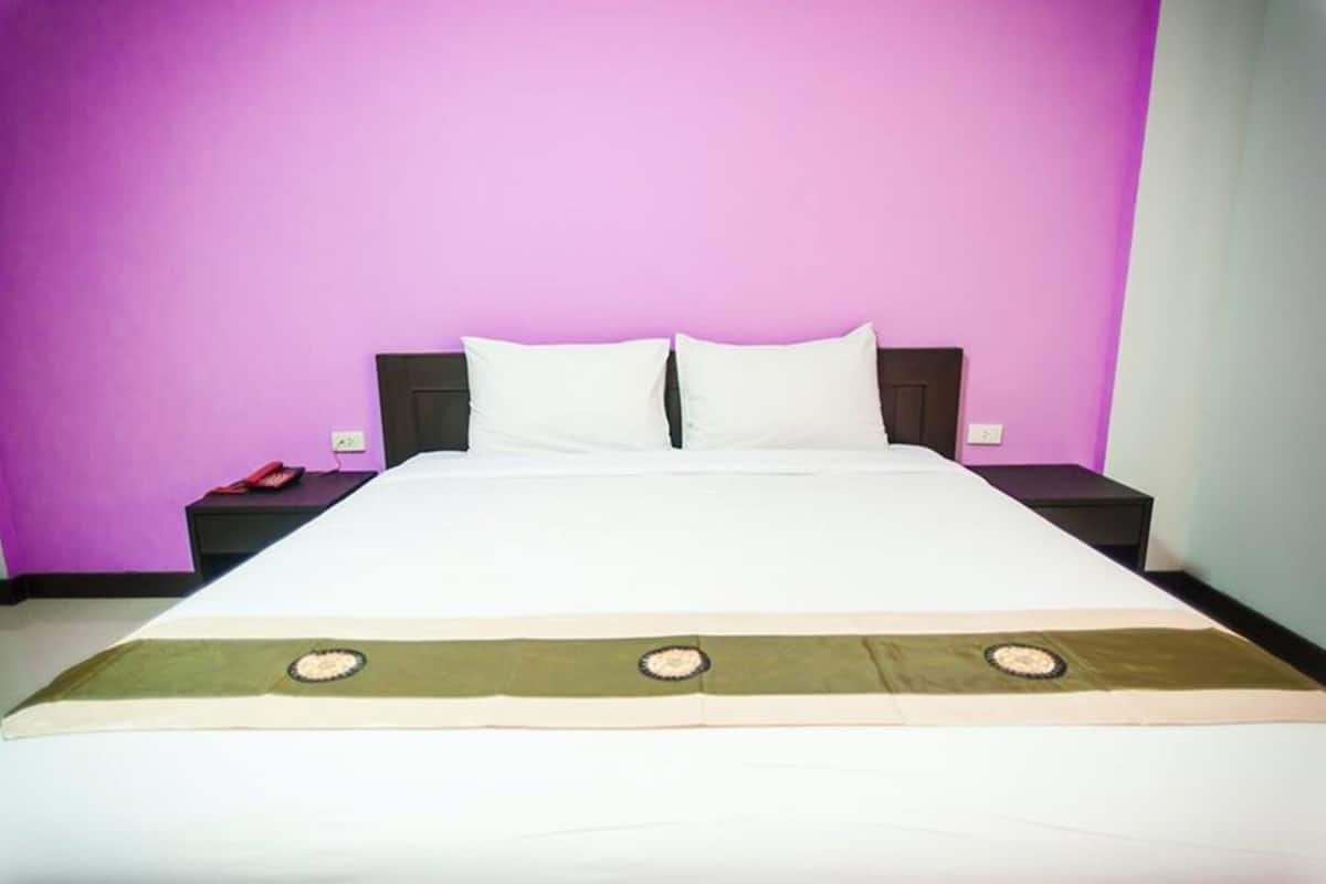 Una cama con ropa blanca, dos almohadas y una colcha verde y beige con diseños circulares.