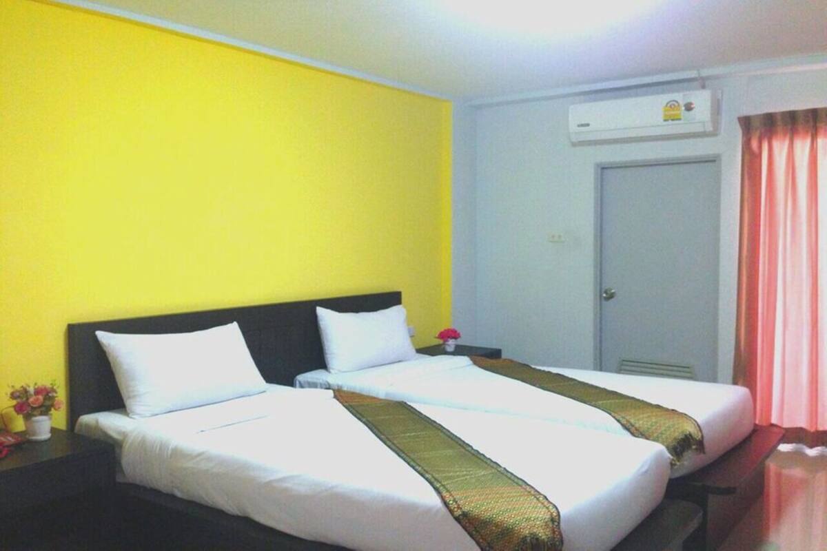 Habitación de hotel con dos camas, una pared blanca, una puerta y un equipo de aire acondicionado.