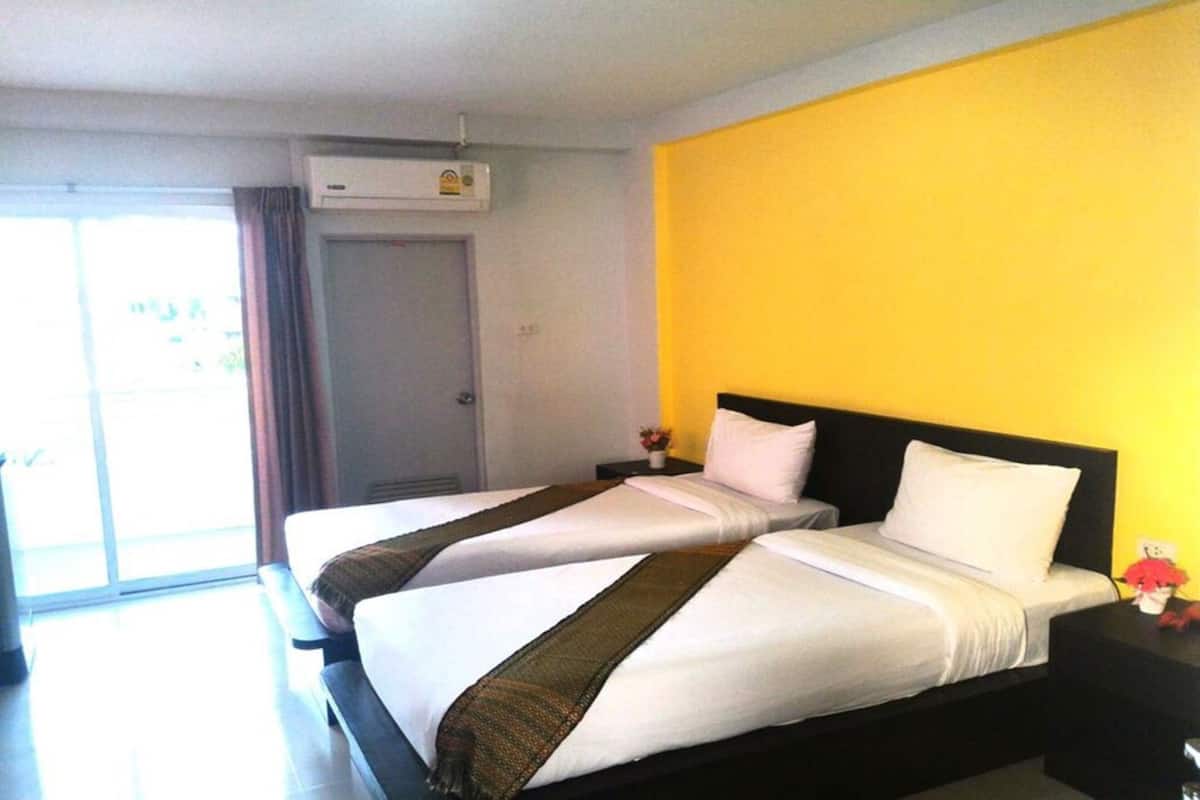 Habitación de hotel con dos camas, una pared de acento amarilla y un ventanal corredizo al exterior.