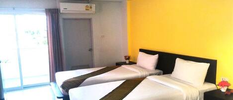 Habitación de hotel con dos camas, una pared de acento amarilla y un ventanal corredizo al exterior.