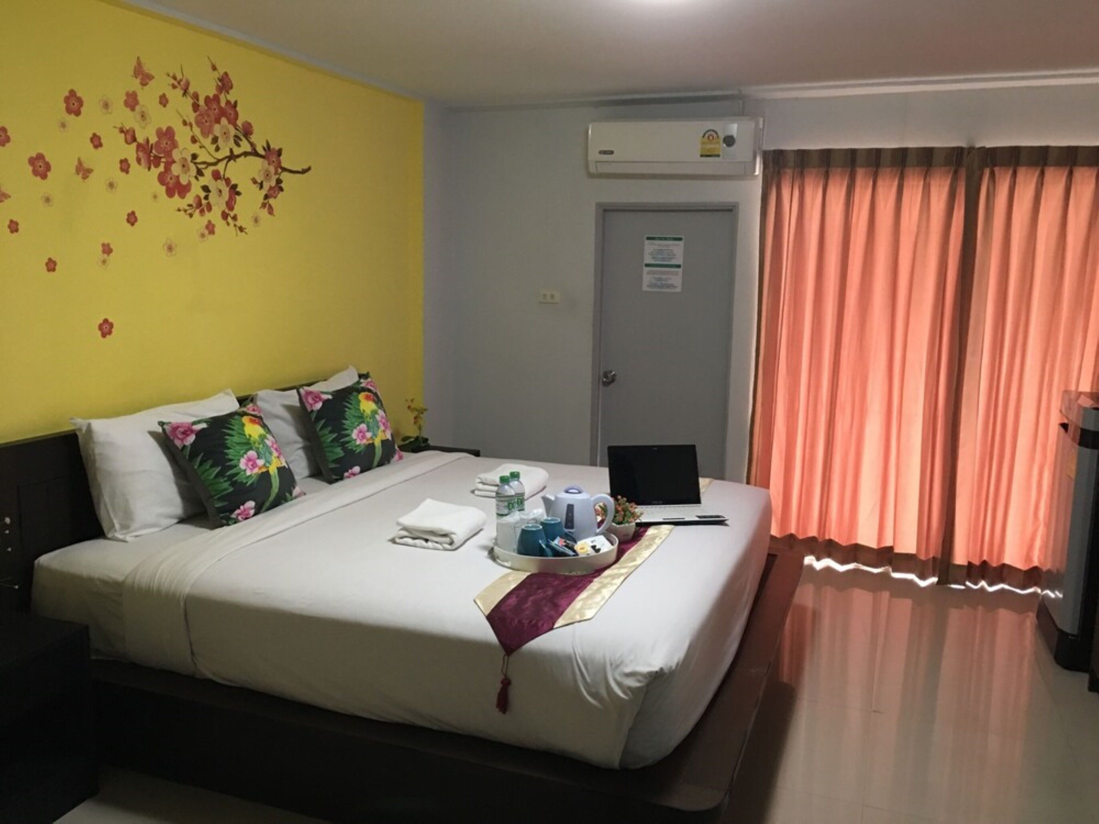 Una camera d'albergo con un letto, cuscini, un laptop e una finestra con tende.