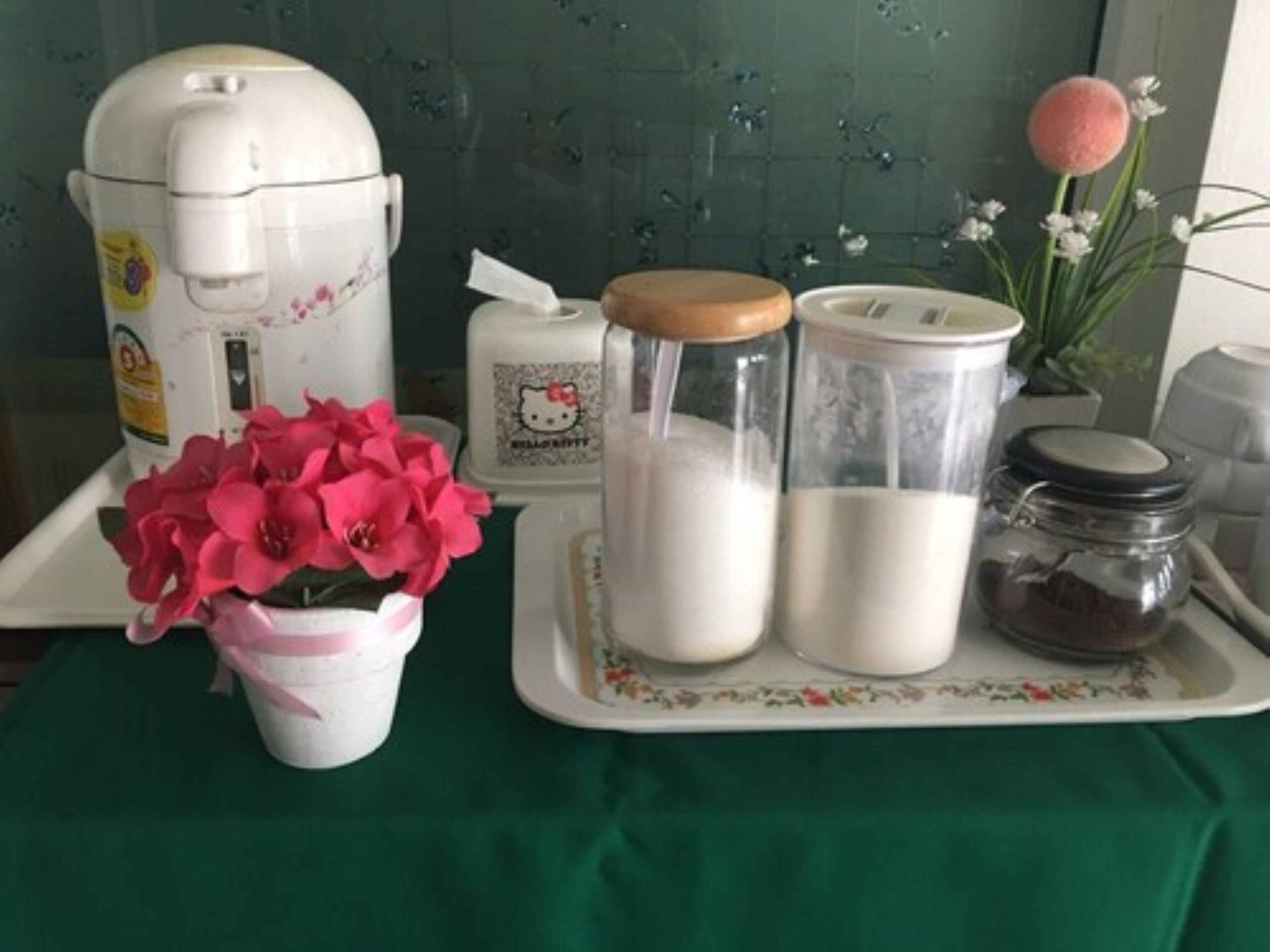 Een keukenblad met een koffiezetapparaat, Hello Kitty-thema potjes, een suikerpot en een vaas met roze bloemen.