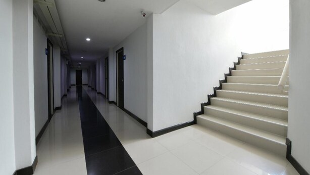A long, narrow hallway with a black and white tiled floor, leading to a beige staircase with black edges.