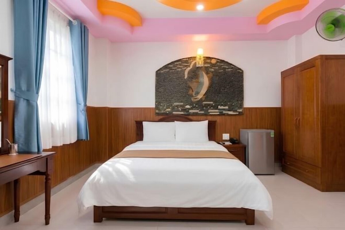 A hotel room with a bed, a desk, a refrigerator, and a wooden wardrobe.