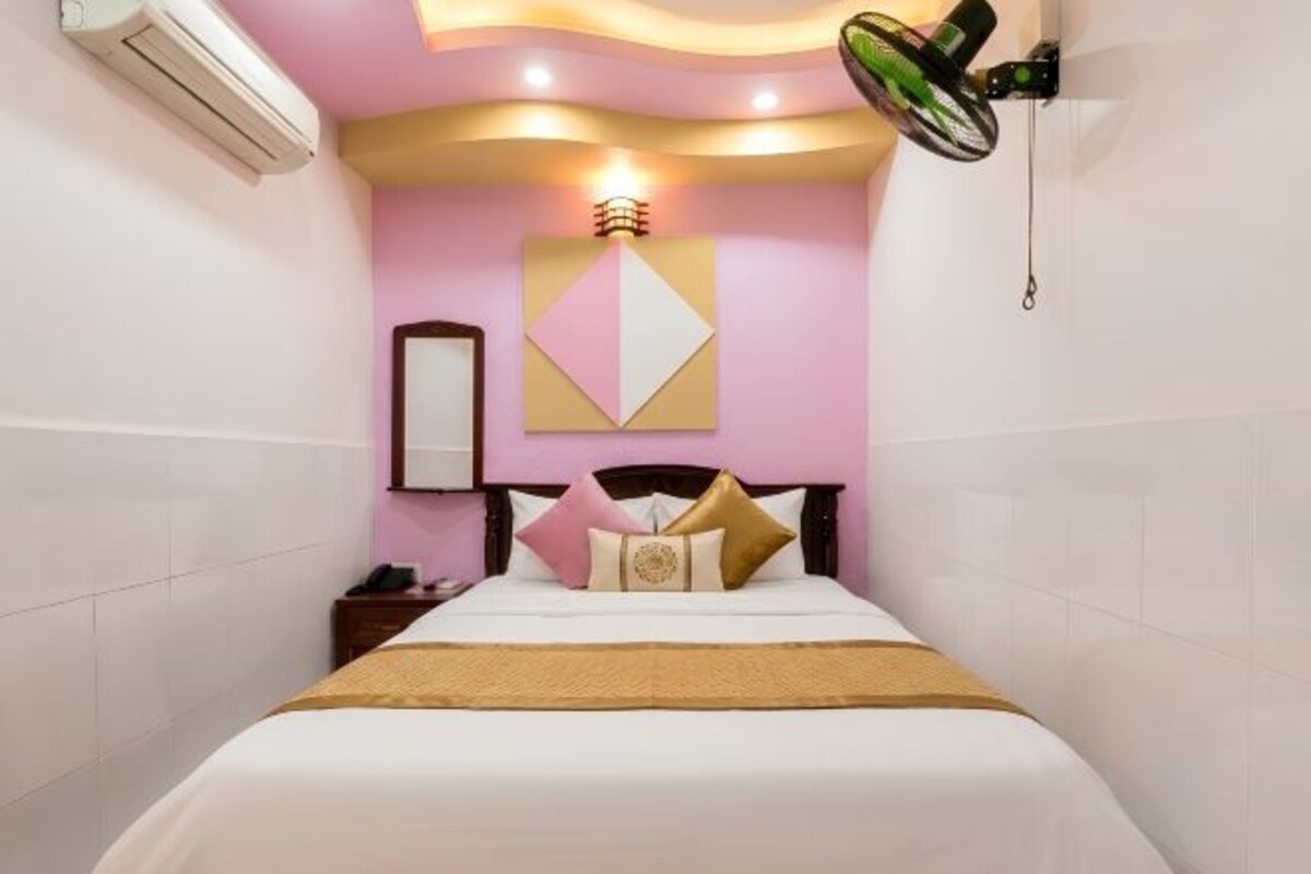 A hotel room with a bed, a nightstand, a wall-mounted air conditioner, and a ceiling fan.