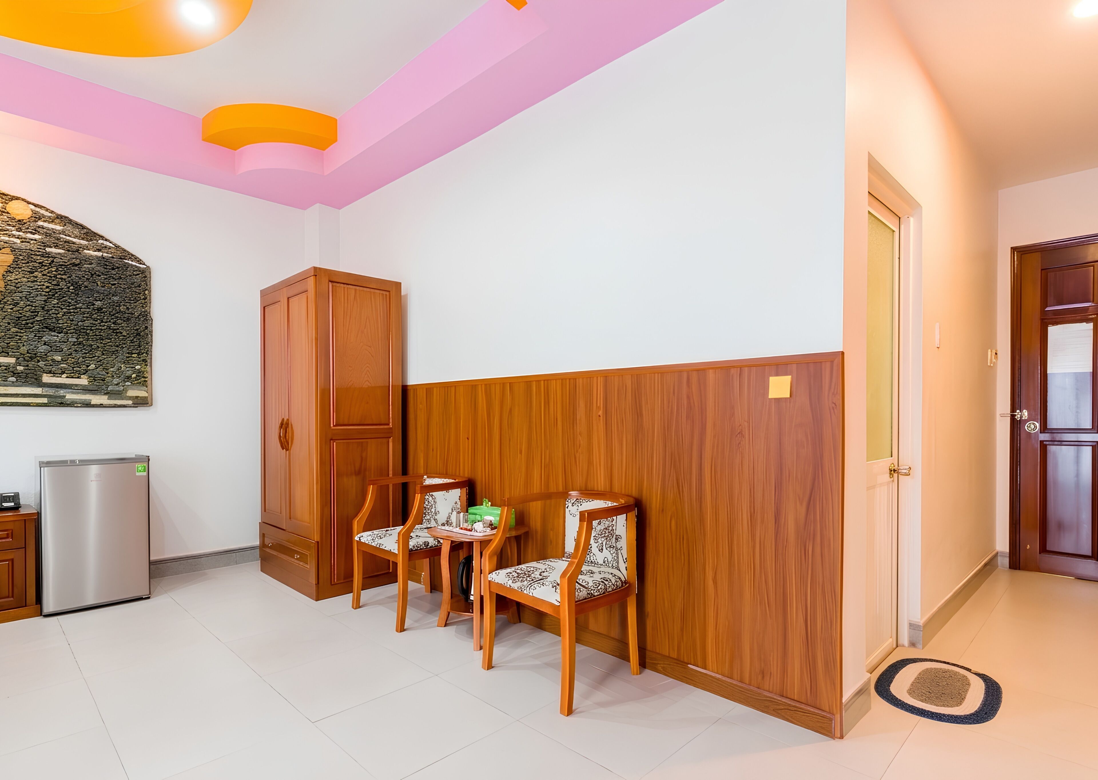 A room with a wooden cabinet, two chairs, a refrigerator, and a door.