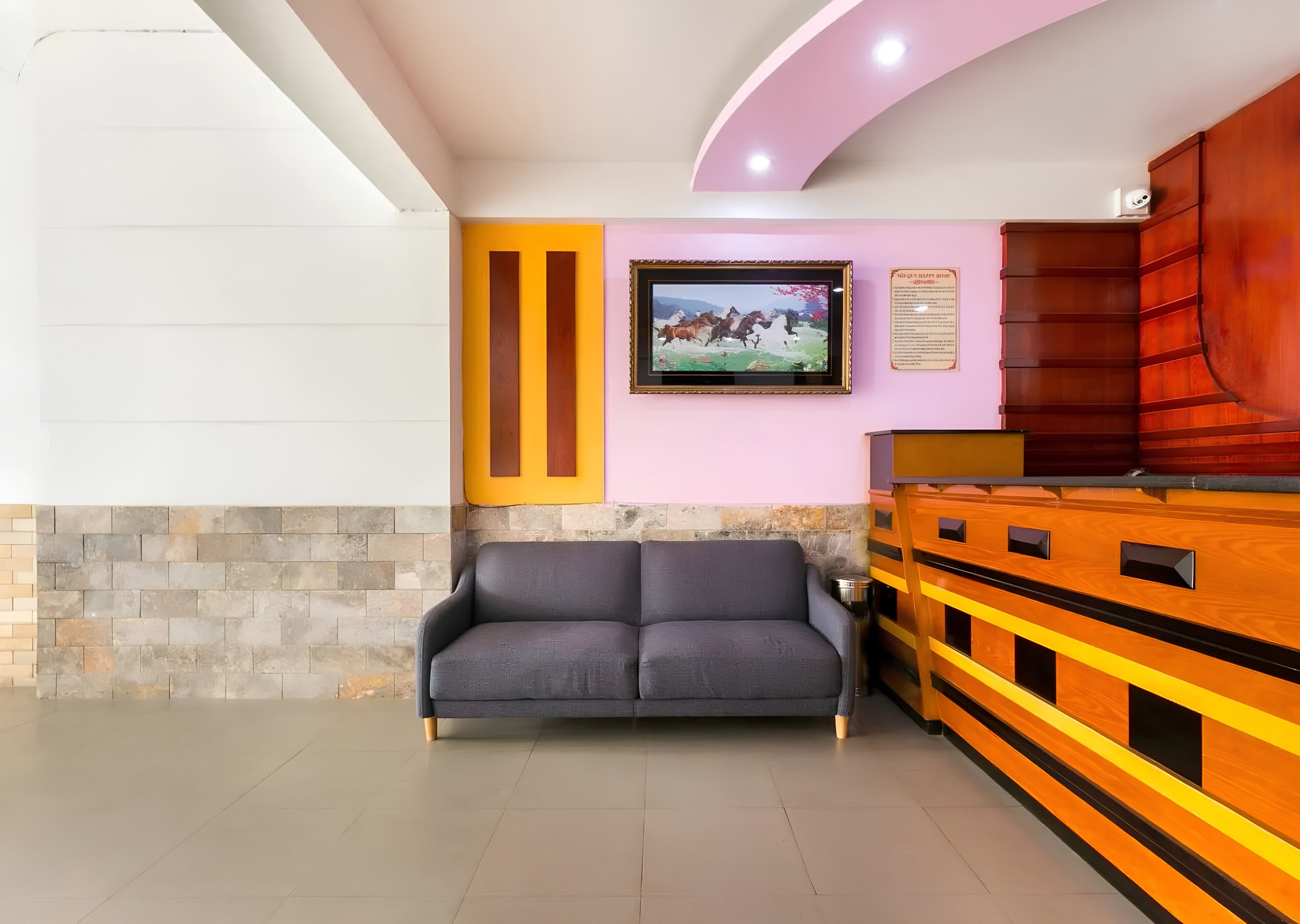 A reception area with a sofa, a television mounted on the wall, and a wooden cabinet with drawers.