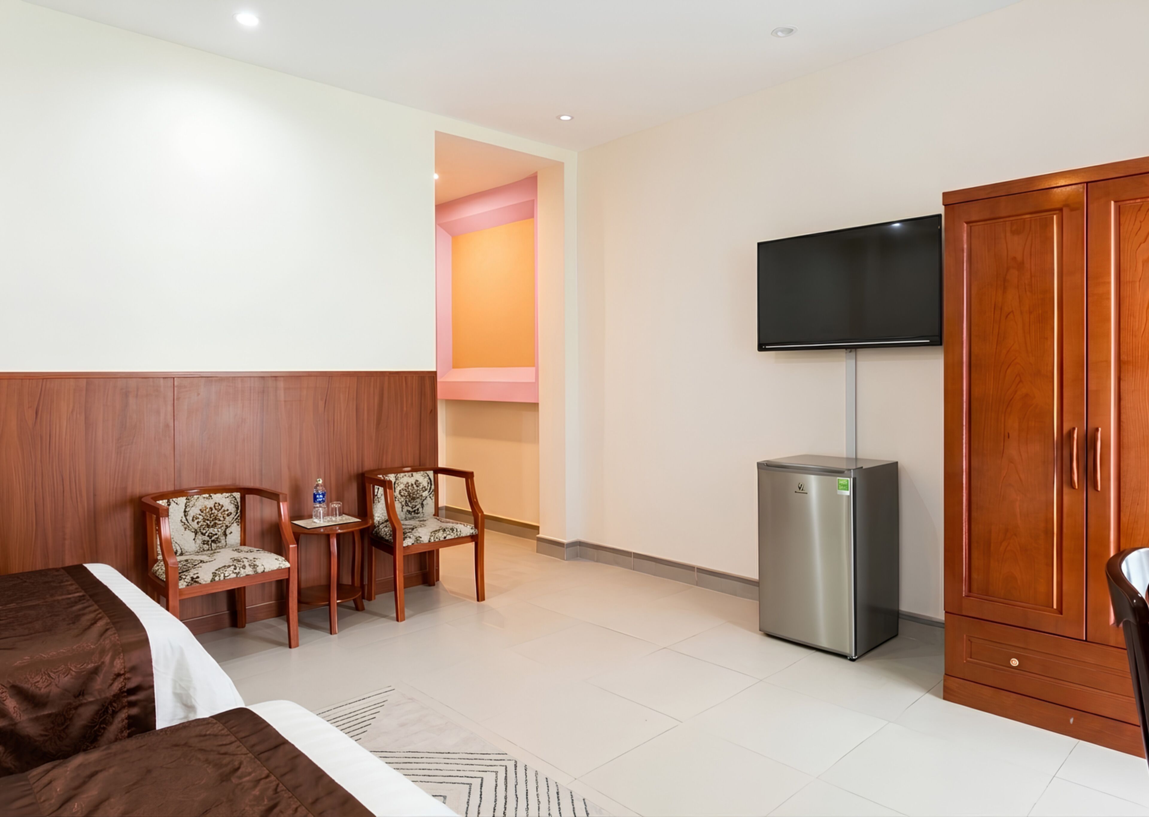 Ein Hotelzimmer mit einem Bett, zwei Stühlen, einem Fernseher, einem Kleiderschrank und einer kleinen Kühlschrank.