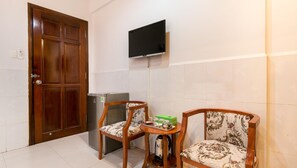 Una habitación compacta con una puerta de madera, un televisor de pantalla plana montado en la pared, un refrigerador, dos sillas con diseño y una pequeña mesa con bandeja.