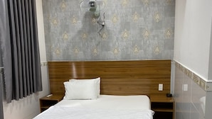 Ein ordentlich bezogenes Bett mit hölzernem Kopfteil, einem Nachttisch, einer Wandleuchte und einer Wand mit grauem Muster.