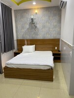 Uma cama bem arrumada com cabeceira de madeira, mesa de cabeceira, luminária fixada na parede e parede com padrão cinza.