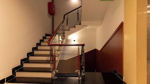 A staircase with a handrail, a red emergency exit sign, and a wooden wall. - Prince Hotel (Ho Chi Minh City)