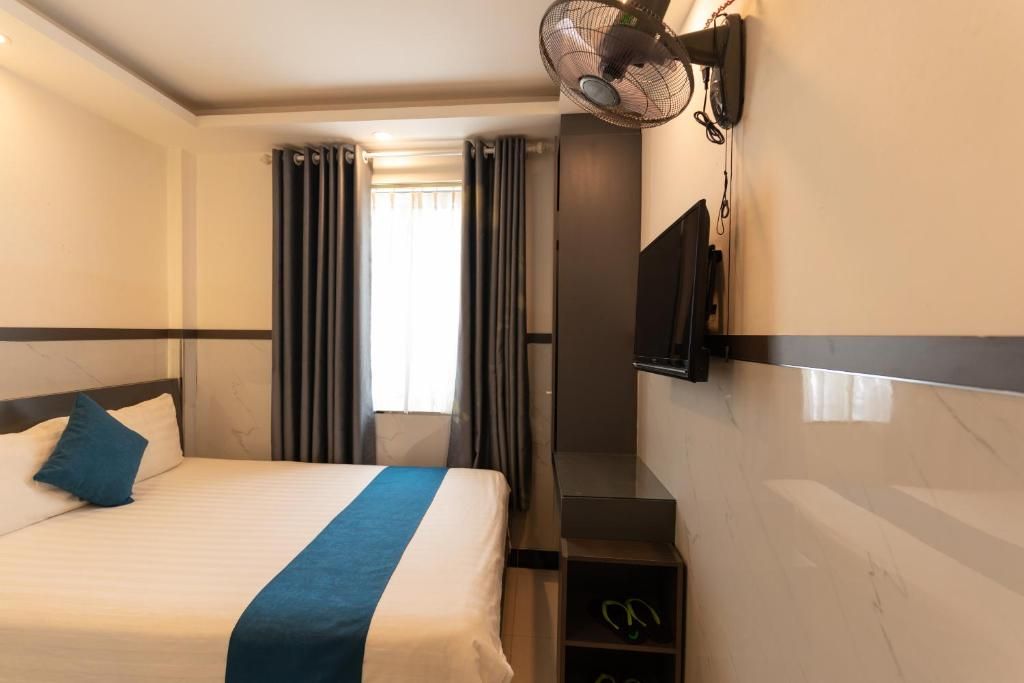 Une chambre d’hôtel avec un lit, une télévision, un ventilateur et une fenêtre avec des rideaux.