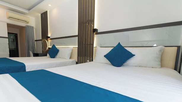 A hotel room with two beds, each with blue bedding and pillows, a large mirror, and a modern design with a marble headboard. - Prince Hotel (Ho Chi Minh City)