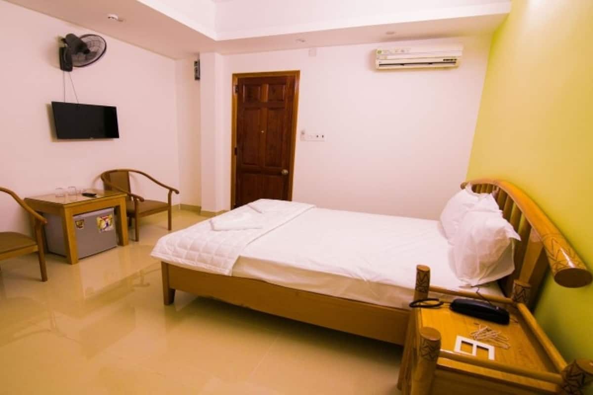 A small, clean room with a bed, a desk, a chair, a fan, and an air conditioning unit.