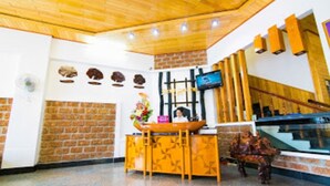 A reception area with a wooden reception desk, a TV mounted on the wall, and a brick wall with decorative elements. - Dong Phuong Hotel (Quy Nhon Nam)