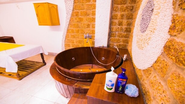 A wooden bathtub in a room with a tiled floor, a wooden cabinet, and a table with a white tablecloth. - Dong Phuong Hotel (Quy Nhon Nam)