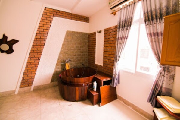 A bathroom with a wooden bathtub, a sink, and a shower area. - Dong Phuong Hotel (Quy Nhon Nam)