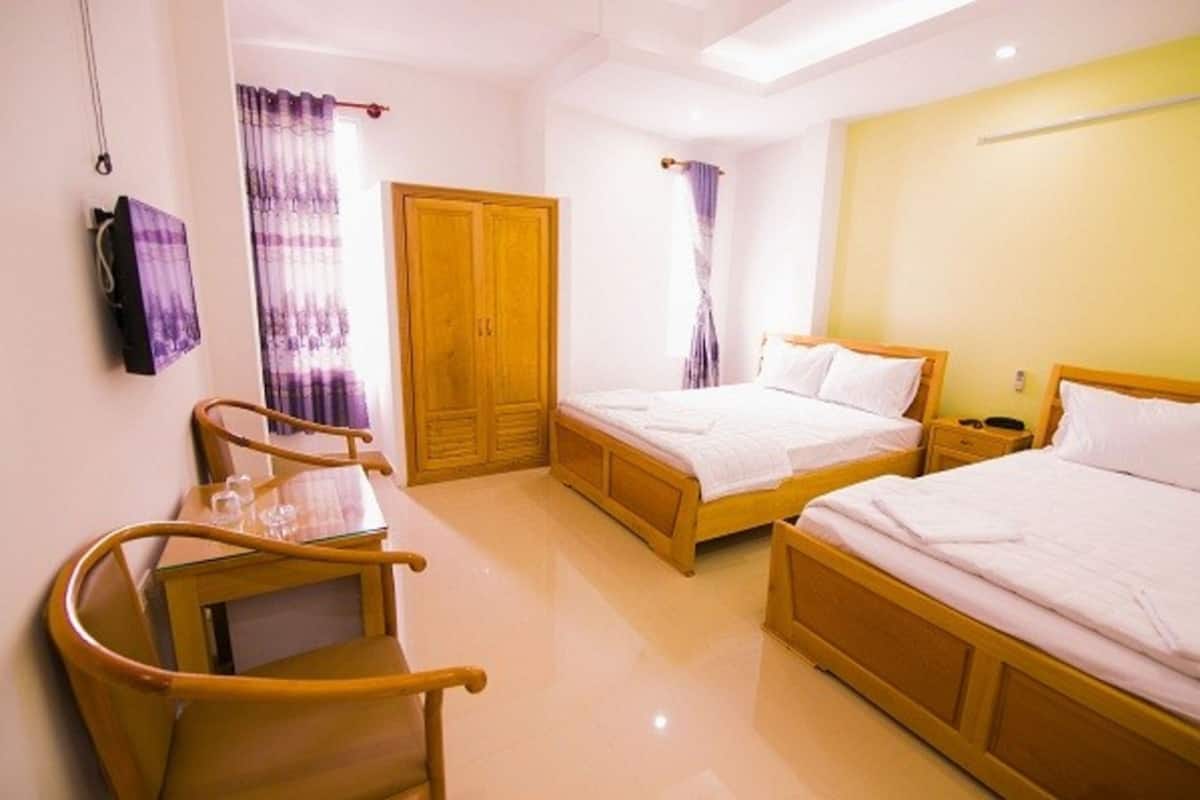 A hotel room with two single beds, a wooden wardrobe, a wooden chair, and a small table with a glass.