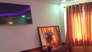 A living room with a checkered floor, a red sofa, a small table with a potted plant, a framed picture, and a television mounted on the wall. - Hoa Anh Dao 2 Hotel (Ho Chi Minh City)