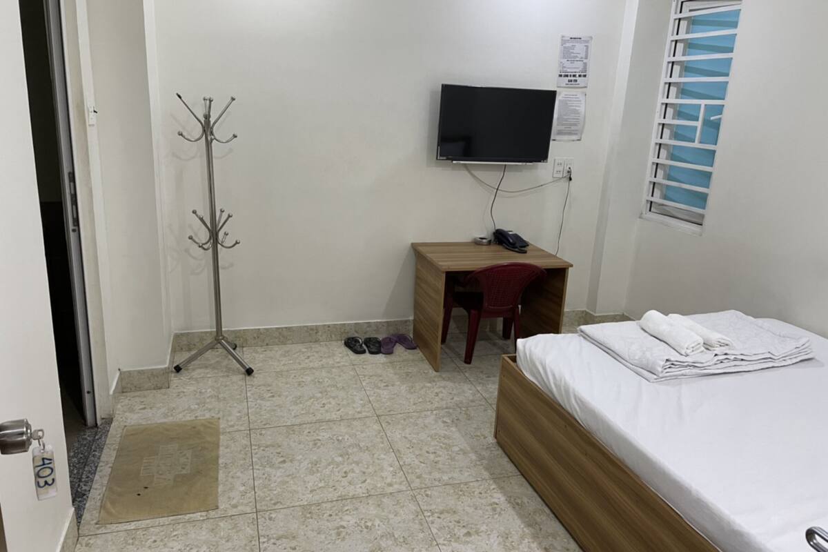 A small, clean room with a bed, a desk, a TV, and a coat rack.
